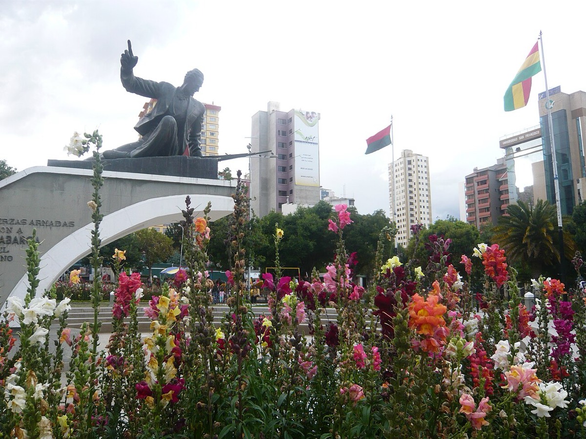 Monumento a Eduardo Abaroa en la plaza Abaroa de La Paz, con flores en primer plano y edificios al fondo